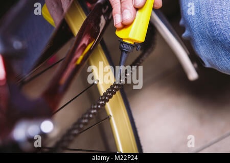 Tema la riparazione di biciclette. Close-up di un uomo caucasico la mano utilizzare un lubrificante per catena in un lubrificatore giallo per llubricator una catena di bicicletta su una bicicletta rossa. Foto Stock
