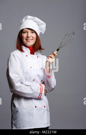 Foto di chef femmina in tunica bianca e il cappuccio con la frusta in mano Foto Stock