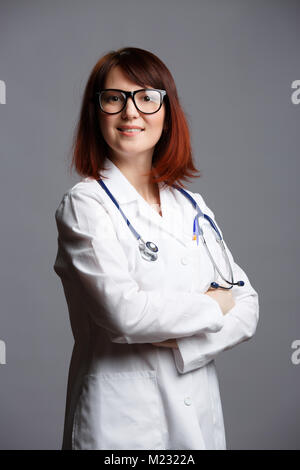 Foto di sorridere medico donna in camice bianco e con phonendoscope in bicchieri Foto Stock