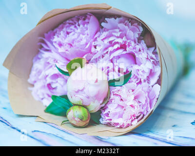 Un mazzo di fiori di un bel colore rosa peonie su un colore bluastro tavola in legno rustico sparato contro soft-focalizzata sullo sfondo. Foto Stock