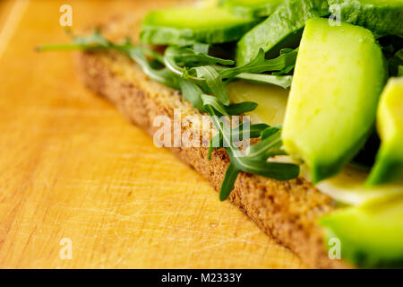 Bruschetta vegetariana con avocado e rucolla od un tavolo di legno. Foto Stock
