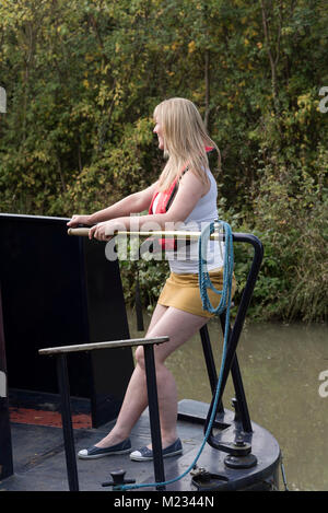 Donna che utilizza il timone e di indossare un giubbotto salvagente la sterzatura di un narrowboat Foto Stock