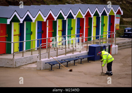 Eliminazione di distanza di sabbia che è stata soffiata oltre la parete del mare durante un forte vento presso il beach hut area a Whitmore Bay, Barry Island Barry Wales Foto Stock