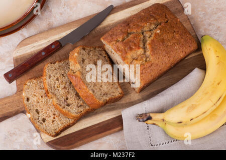 Dado di banana a fette di pane su un tagliere di legno con banane sul lato Foto Stock