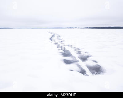 Fuso motoslitta scuro tracce su una congelati coperta di neve sul lago. Tartu, Estonia. Foto Stock