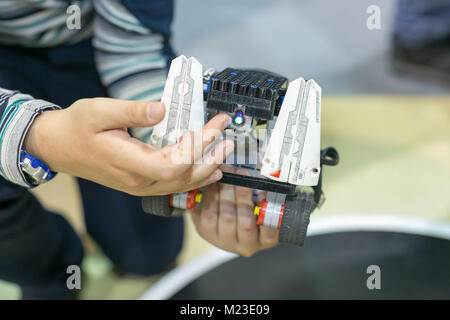 Robotics, intrattenimento, infanzia concetto. nelle braccia di piccolo ragazzo vi è il robot fatto di pezzi di lego, ruote e dettagli elettrici di controllo Foto Stock