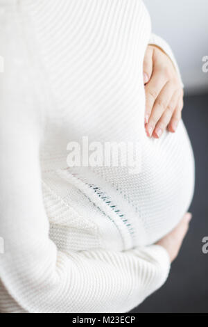 Futuro, gravidanza, maternità concetto. vi è una stretta dei giovani womans mani sul suo ventre coperto con maglia maglione, è incinta che è il motivo per cui lei è teneramente abbraccia il suo ventre Foto Stock