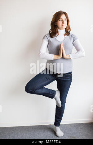 Sanità, sport, bambino nascita concetto. vi è giovane e donna incinta, che sono vestiti di stretching jeans e maglione grigio, sta facendo esercizi fisici di yoga Foto Stock