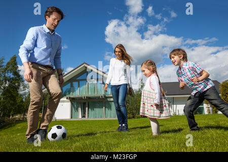 Famiglia con bambini che giocano a calcio sul prato vicino a casa loro Foto Stock