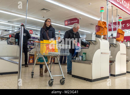 Donna con carrello e i clienti pagano per i loro acquisti presso il self checkout area di Sainsbury's supermercato di Bourne, Lincolnshire, Inghilterra, Regno Unito. Foto Stock