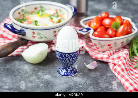 Uova sode nel supporto con pomodoro e shakshuka su di un legno grigio tavolo rustico Foto Stock