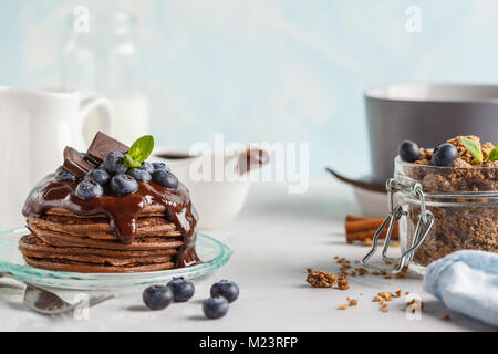 Frittelle di cioccolato con sciroppo e frutti di bosco, cioccolato granola, latte e uova. Concetto di colazione Foto Stock