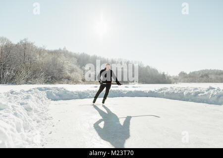 Uomo in azione la riproduzione di hockey su ghiaccio su un luminoso giorno Foto Stock