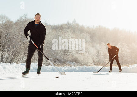 Due uomini giocare hockey su ghiaccio su un lago ghiacciato Foto Stock