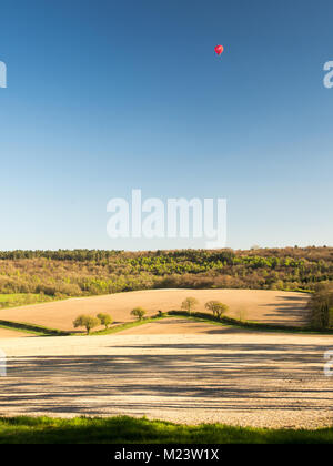 Una mongolfiera galleggia sul Wendover boschi e campi arati in Hale in Inghilterra del Chiltern Hills. Foto Stock