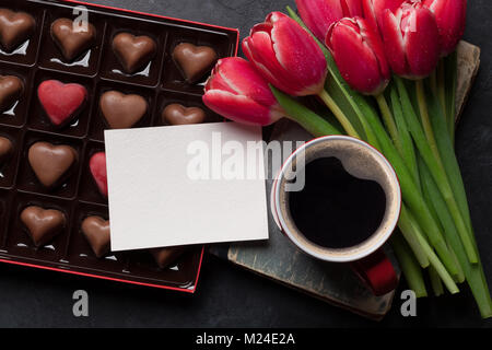 Red tulip bouquet di fiori, la tazza di caffè e cioccolato cuori in confezione regalo. Il giorno di San Valentino biglietto di auguri. Vista da sopra con lo spazio per i messaggi di saluto Foto Stock