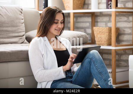 Sorridente bella donna con tavoletta digitale in casa Foto Stock