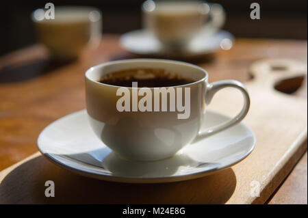 Tazza di caffè appena fatto su uno sfondo sfocato di due tazze. Tavolo in legno nella camera. Foto Stock