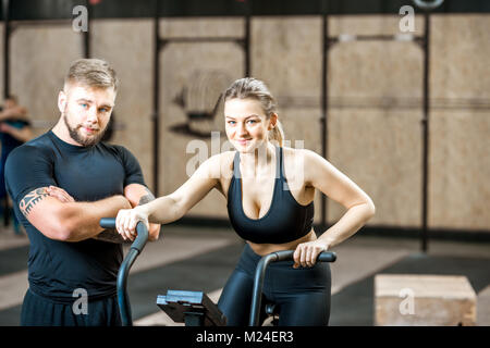 Donna formazione sulla cyclette con trainer in palestra Foto Stock