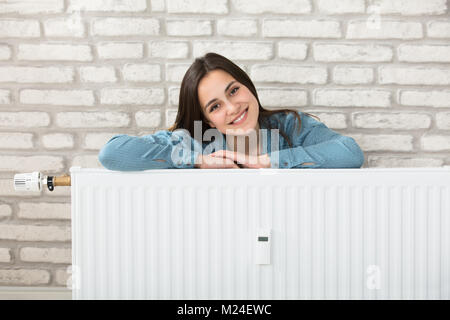 Ritratto di una donna sorridente dietro il radiatore di riscaldamento Foto Stock