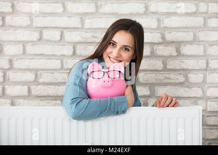 Ritratto di una donna sorridente dietro il radiatore di riscaldamento Azienda Salvadanaio Foto Stock