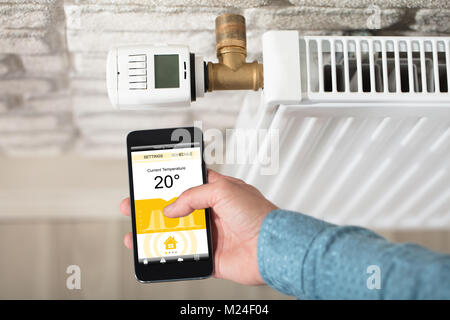 Close-up di mano di una persona la regolazione della temperatura sul termostato attraverso il telefono cellulare Foto Stock