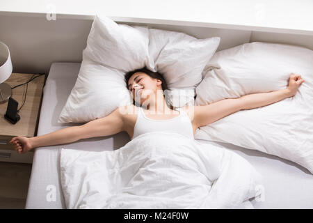 Vista in elevazione di una giovane donna lo stiramento delle sue mani sul letto Foto Stock