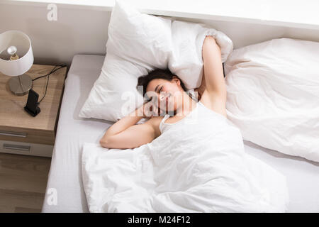 Vista in elevazione di una giovane donna lo stiramento delle sue mani sul letto Foto Stock