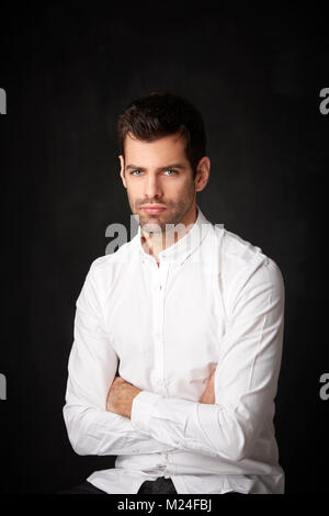 Casual giovane con bracci ripiegati seduta a sfondo scuro con copia spazio. Foto Stock