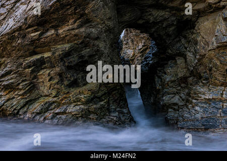 Acqua di mare va in crash attraverso il foro per la chiave apertura sagomata in una scogliera a sputare Beach in St Austell Cornwall. Foto Stock