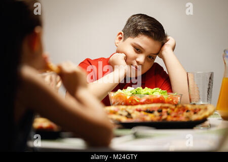 Madre dando invece Insalata di Pizza al Figlio in sovrappeso Foto Stock