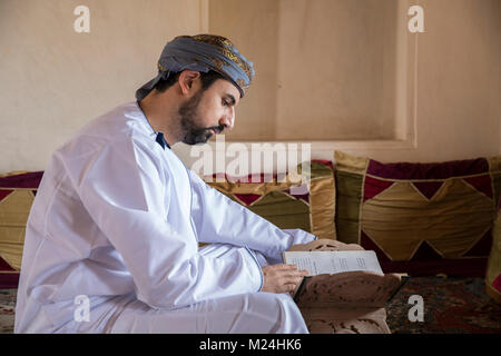 Omani uomo in abito tradizionale la lettura di un libro Foto Stock