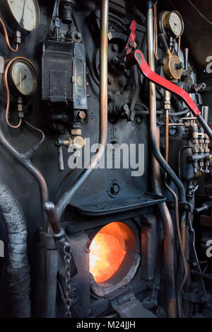 Formato verticale dell'interno dei comandi di guida su una vecchia locomotiva a vapore treno con la scatola di fuoco aperto che mostra le fiamme Foto Stock