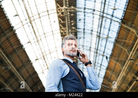 Imprenditore maturo con smartphone in una stazione ferroviaria. Foto Stock