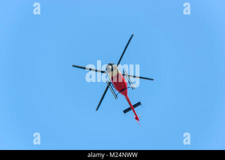 Il bianco e il rosso elicottero in volo contro il cielo blu Foto Stock