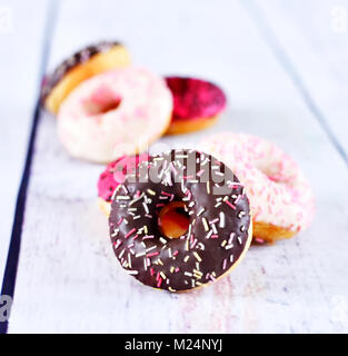 Deliziose le ciambelle con smalto o glassa e spruzza. variazione di ciambelle fresche su un bianco tavolo di legno. Disposizione con copia spazio. Foto Stock