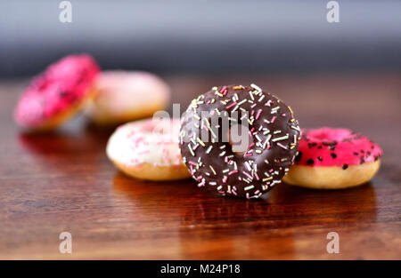 Al delizioso cioccolato ciambelle fresche o ciambella con smalto o glassa e spruzza. Variazione o disposizione di cibo dolce su un tavolo in legno.malsano mangiare Foto Stock