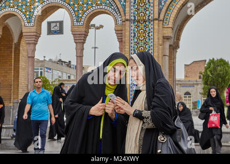 Tehran, Iran - 27 Aprile 2017: due donne iraniane in hijabs stand e guardare foto su uno smartphone vicino lo Shah Abdol Azim Santuario. Foto Stock