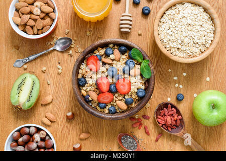 Una sana prima colazione il cibo sulla tavola di legno. Muesli, avena, noci, miele e frutta fresca. Tabella vista superiore Foto Stock