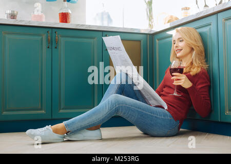 Ispirato donna leggendo un giornale sul pavimento Foto Stock