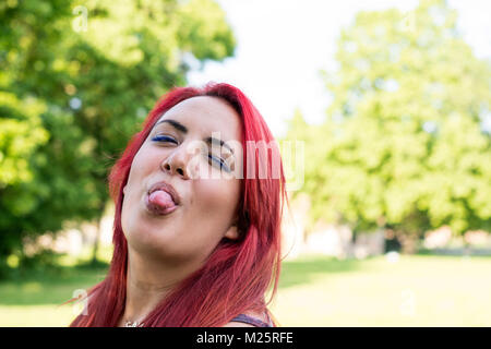 Adolescente arrabbiato con la lingua di fuori trascorrere il suo tempo libero in un parco in estate nel pomeriggio Foto Stock