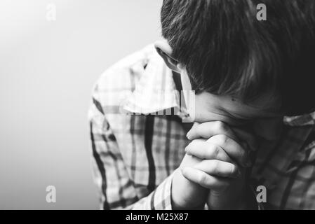 Un giovane ragazzo con la testa piegata nella preghiera. Foto Stock