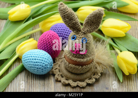 Crochet Easter Bunny egg cup e uova di pasqua di lana. sfondo mazzo di tulipani gialli Foto Stock