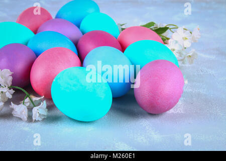 Colorate le uova di pasqua con fiori di colore bianco su un cemento grigio sfondo Foto Stock