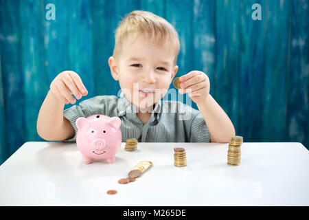 Tre anni bambino seduto st la tabella con i soldi e un piggybank Foto Stock