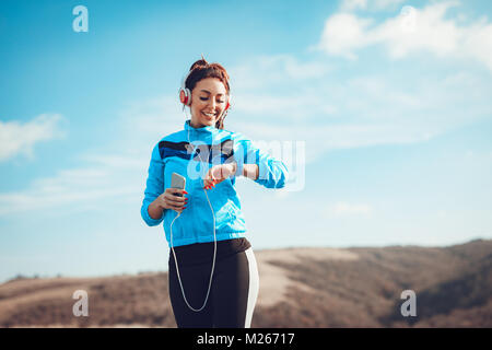 Giovane donna sportivo con le cuffie cercando su un cronometro prima della formazione in natura. Foto Stock