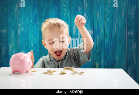 Due anni bambino seduto sul pavimento e mettere una moneta in un piggybank Foto Stock