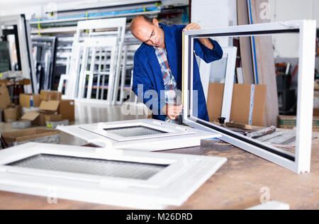 Diligente caposquadra positivo con gli appunti in mani il controllo della qualità dei prodotti finiti di finestre in PVC in fabbrica Foto Stock