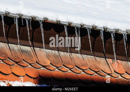 Lunghi ghiaccioli pendenti dal tetto innevate fino al rosso dei pannelli del tetto in corrispondenza di una vecchia casa cittadina in Kaufbeuren, Bavaria Foto Stock