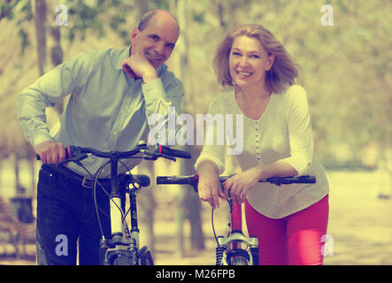 Sorridente coppia internazionale di pensionati attivi con bici all'aperto nella giornata di sole Foto Stock